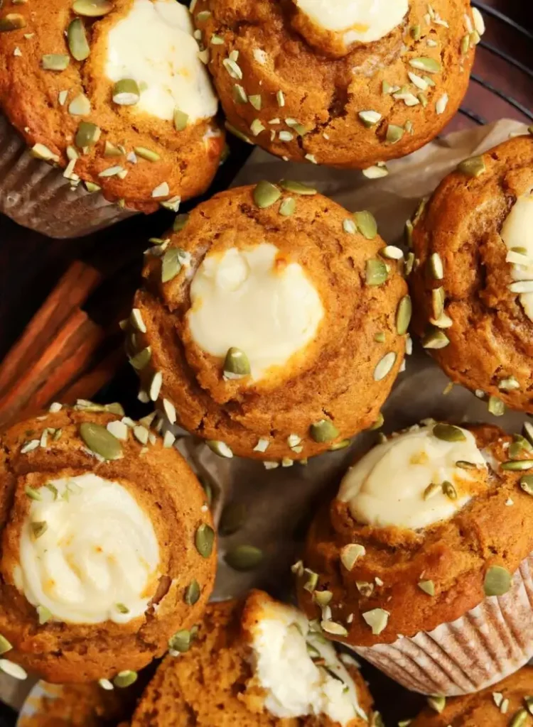 Pumpkin cream cheese swirl muffins, golden brown with a delicious creamy swirl in the center, placed on a rustic wooden table